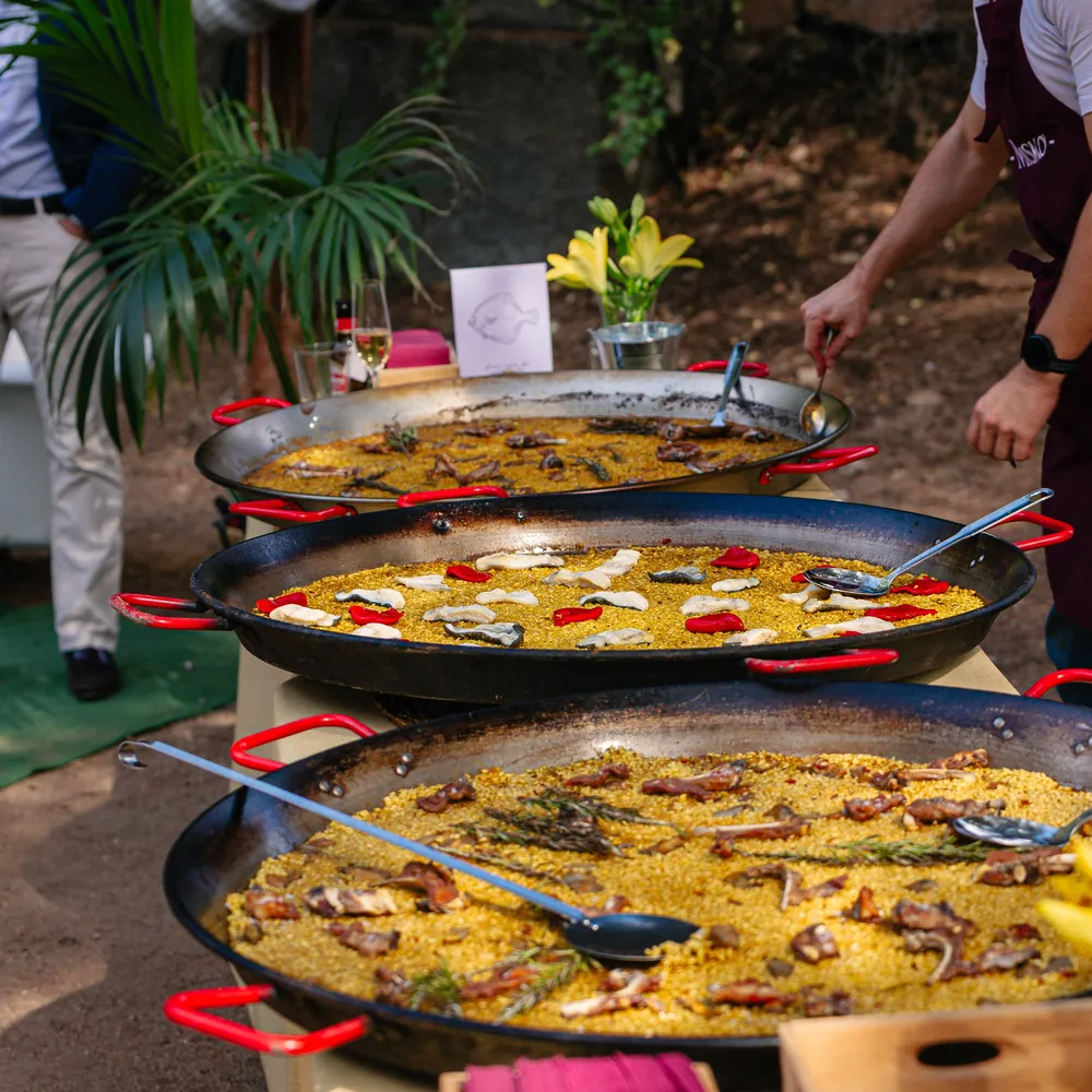 Tres paellas de arroz en fila, con un jarrón de lirios amarillos detrás