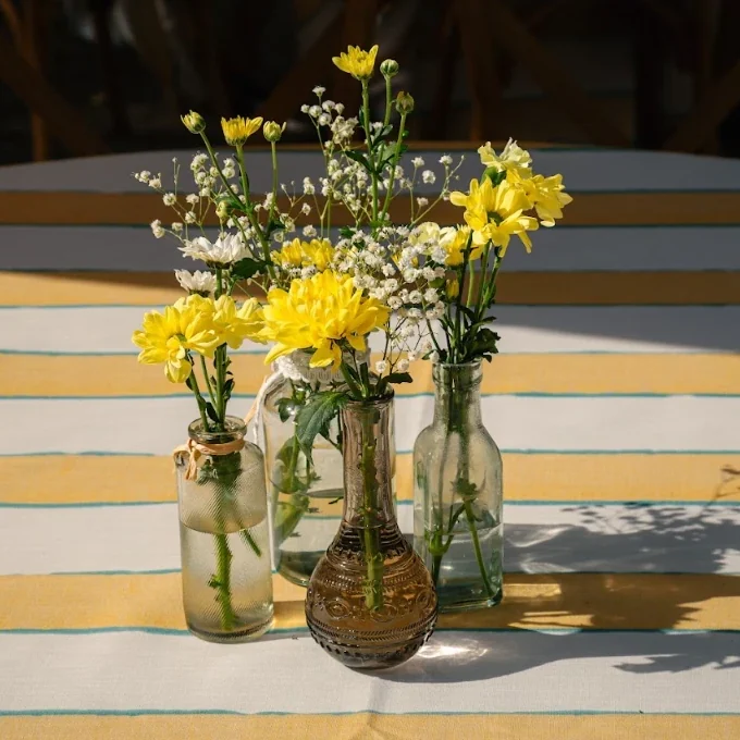Jarrones de cristal con flores amarillas y blancas sobre una mesa con mantel de rayas amarillas