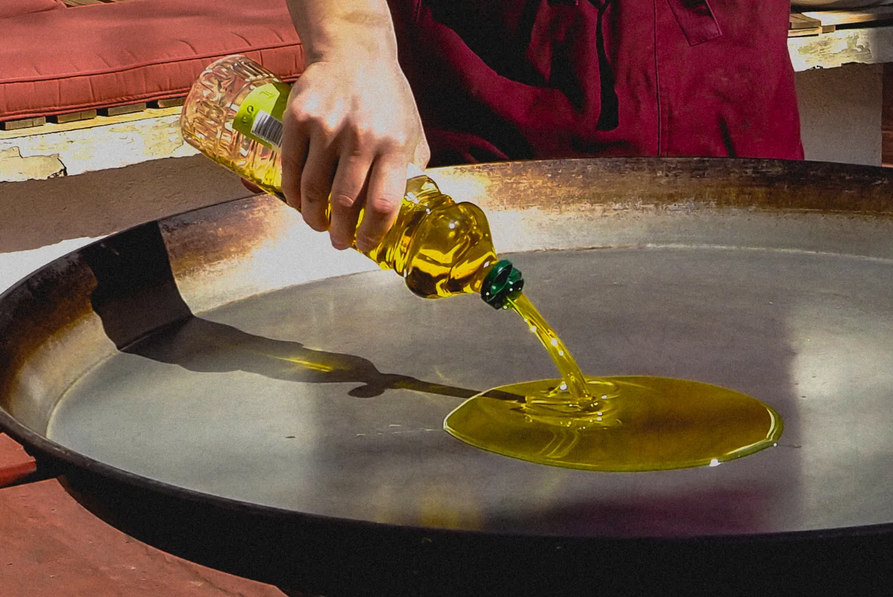 Una mano echa aceite en una paellera grande, todavía vacía, antes de empezar el arroz