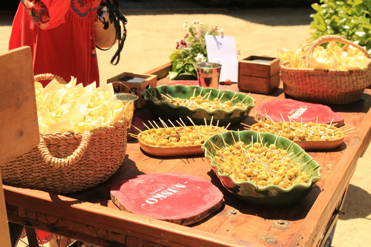 Mesa de madera al aire libre con banderillas en cuencos de cerámica, cestas de patatas fritas y un ramo de flores