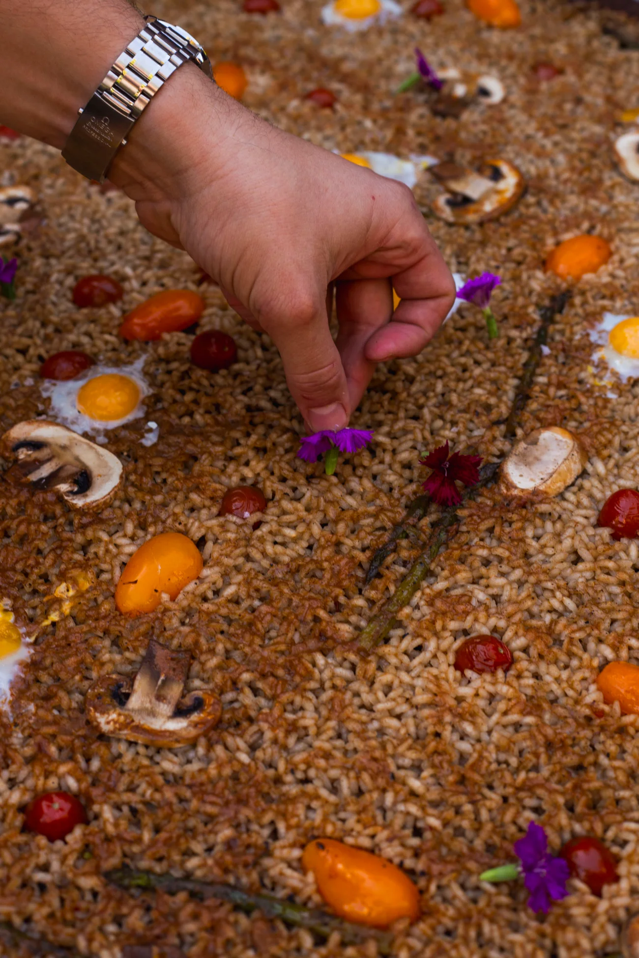 Una mano colocando flores comestibles sobre el arroz, una a una